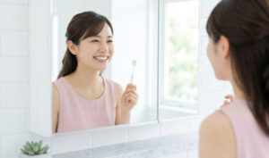 明るい洗面所で、鏡に向かって丁寧に歯磨きをして晴れやかな笑顔を浮かべる日本人女性の様子