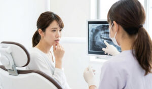 歯科医院で親知らずの抜歯について不安げに相談する日本人女性。歯科医師が優しく対応している様子。
