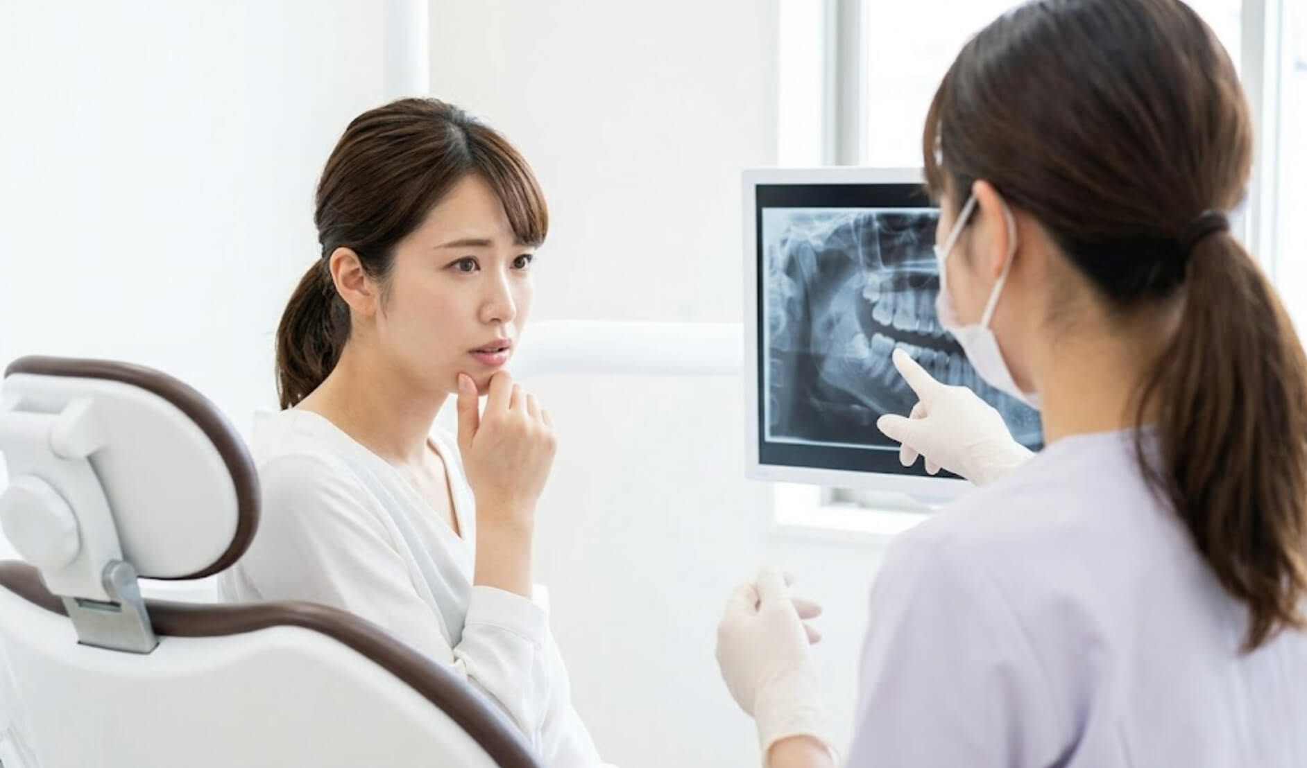 歯科医院で親知らずの抜歯について不安げに相談する日本人女性。歯科医師が優しく対応している様子。